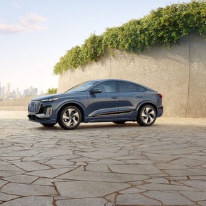 Side-view of the Audi Q6 Sportback e-tron parked with a cityscape in the background.